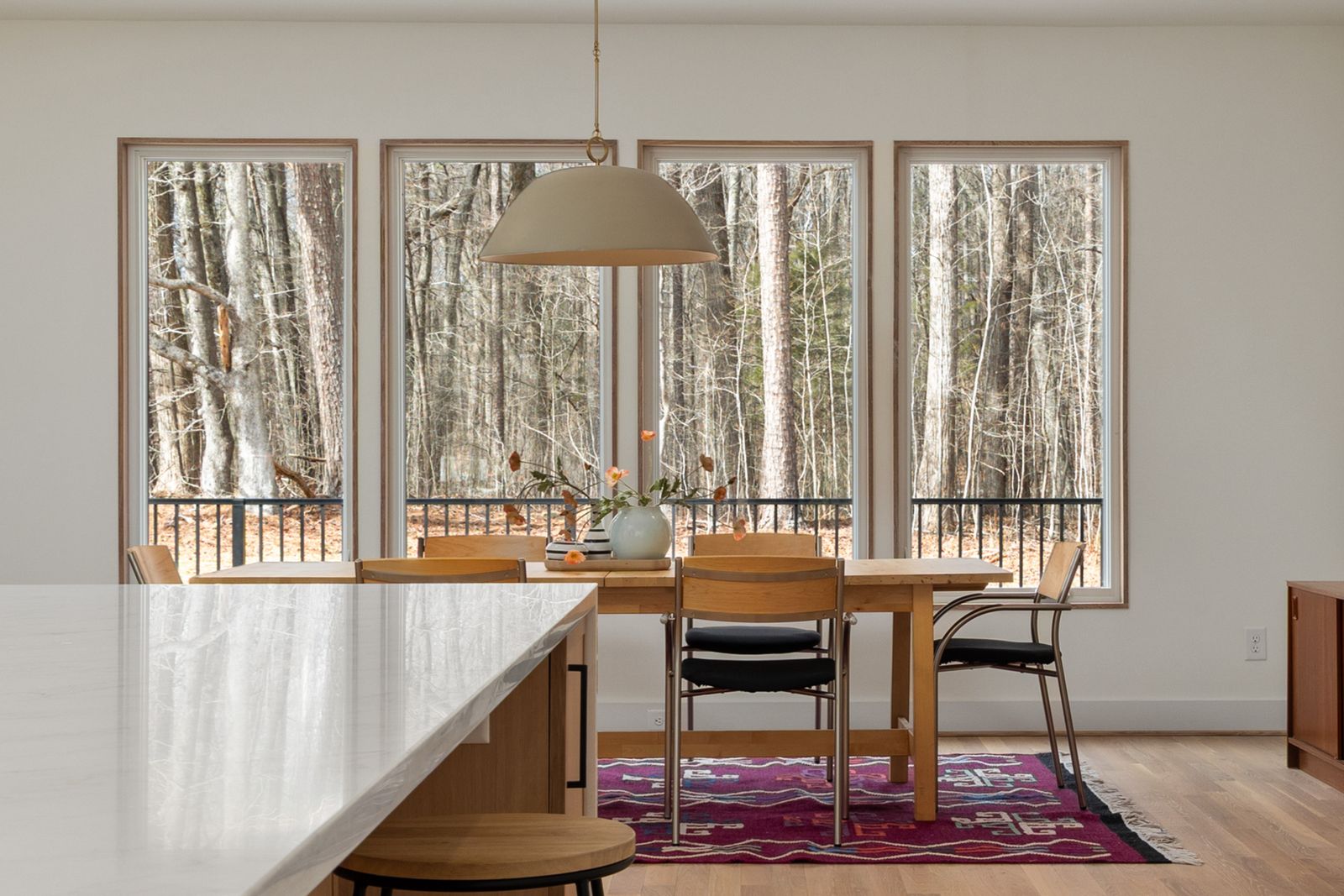 A dining room framed by a wall of tall windows onto bare winter trees.