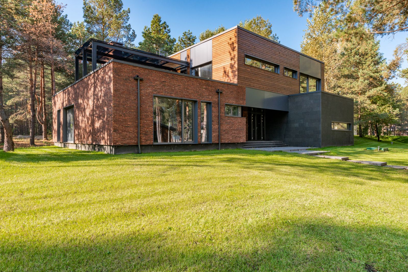 A brick home with wide glazed openings behind a green lawn.