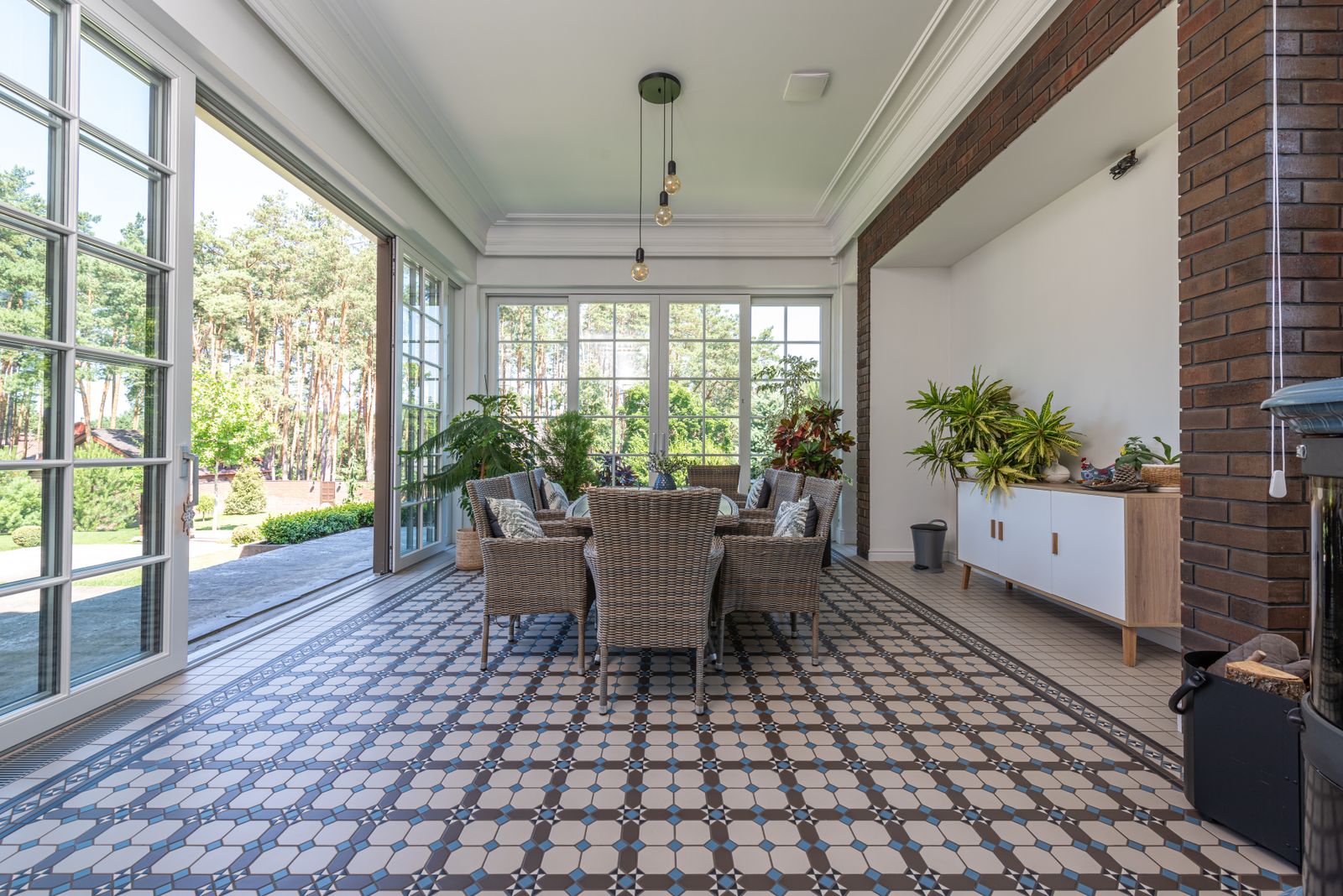 A bright sunroom lined with white-framed windows and a patterned tile floor.